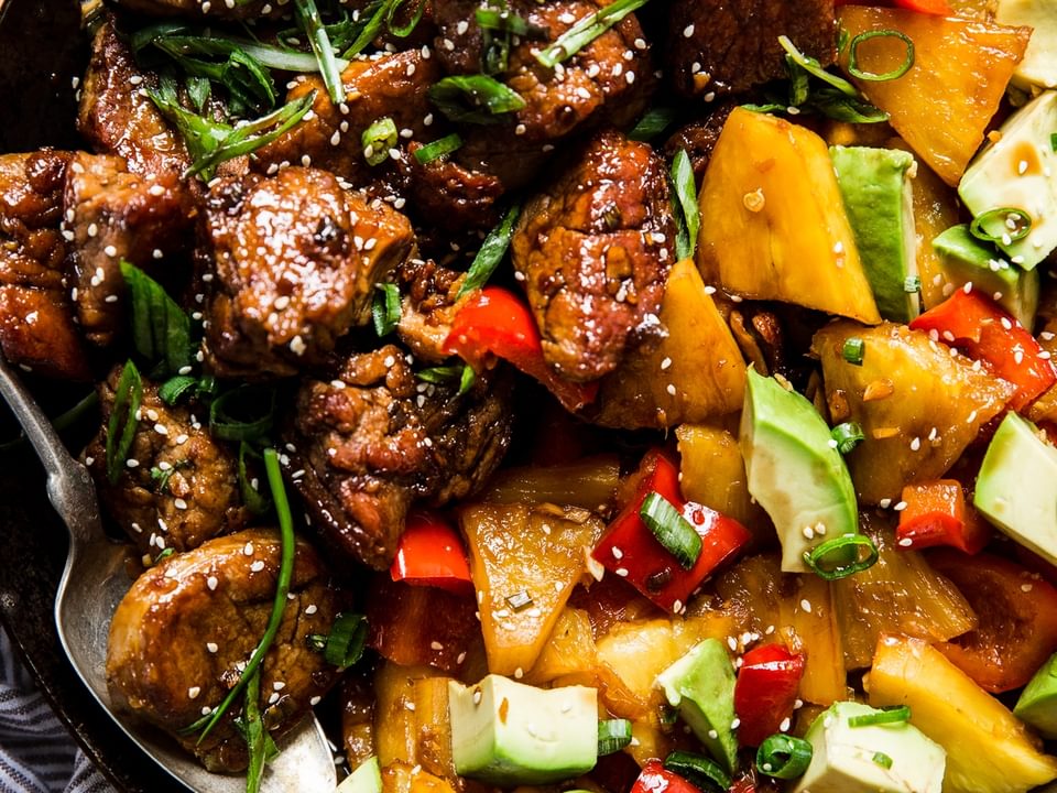 Pineapple Pork Stir Fry with red bell peppers and avocado in a skillet