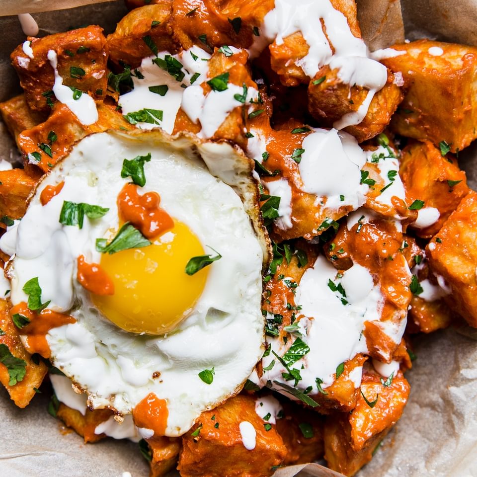 Potatoes bravas in a pan with a fried egg