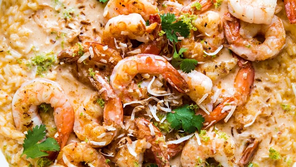 red curry risotto in a white skillet topped with crispy whole shrimp, fresh cilantro and toasted coconut