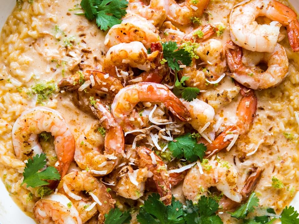 red curry risotto in a white skillet topped with crispy whole shrimp, fresh cilantro and toasted coconut