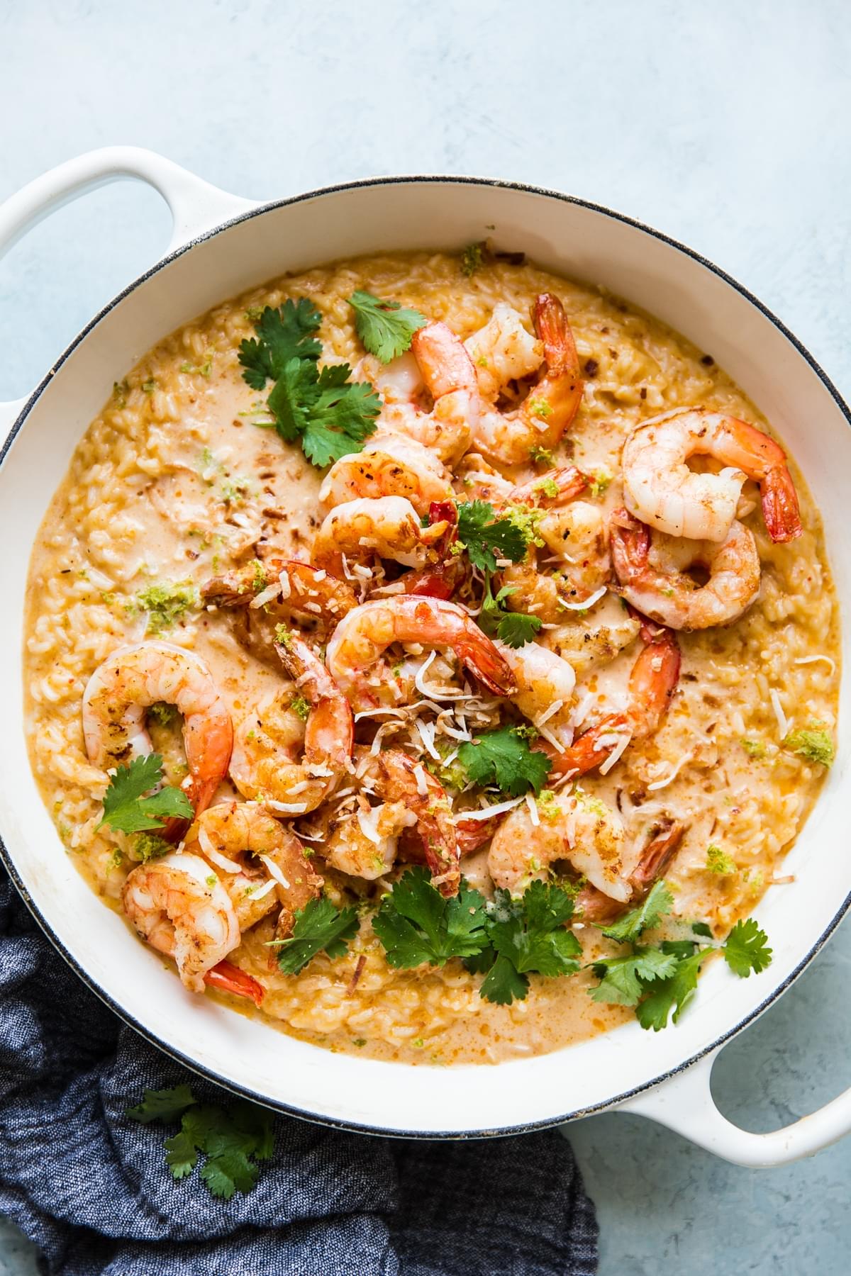 creamy red curry risotto in a skillet topped with shrimp and fresh cilantro