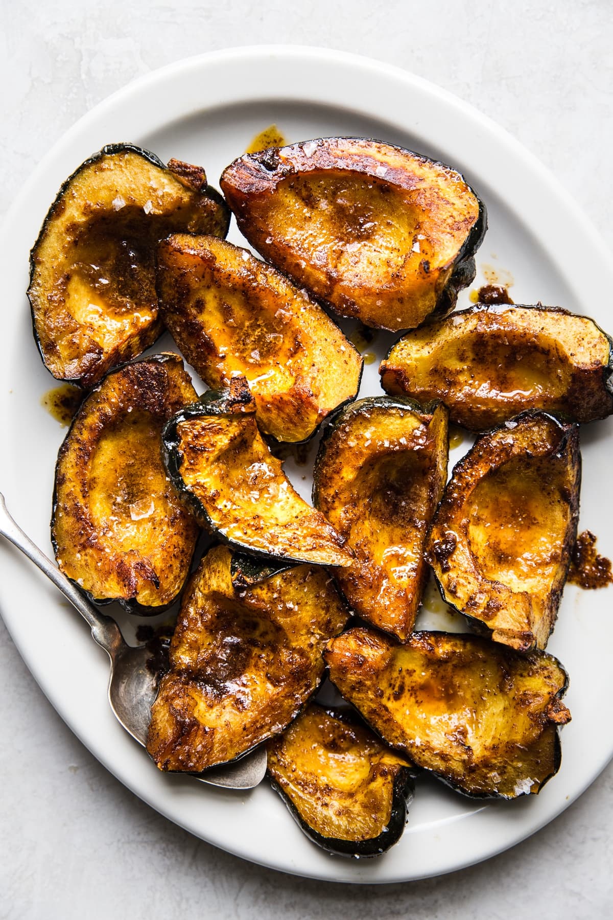 quartered roasted acorn squash on a white platter with a serving spoon