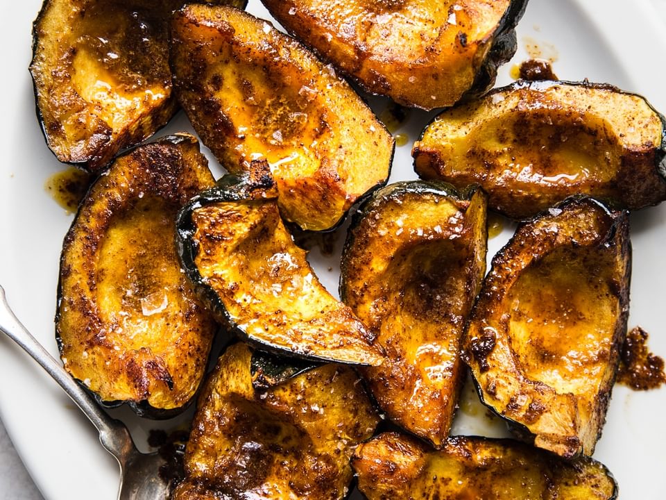 quartered roasted acorn squash on a white platter with a serving spoon