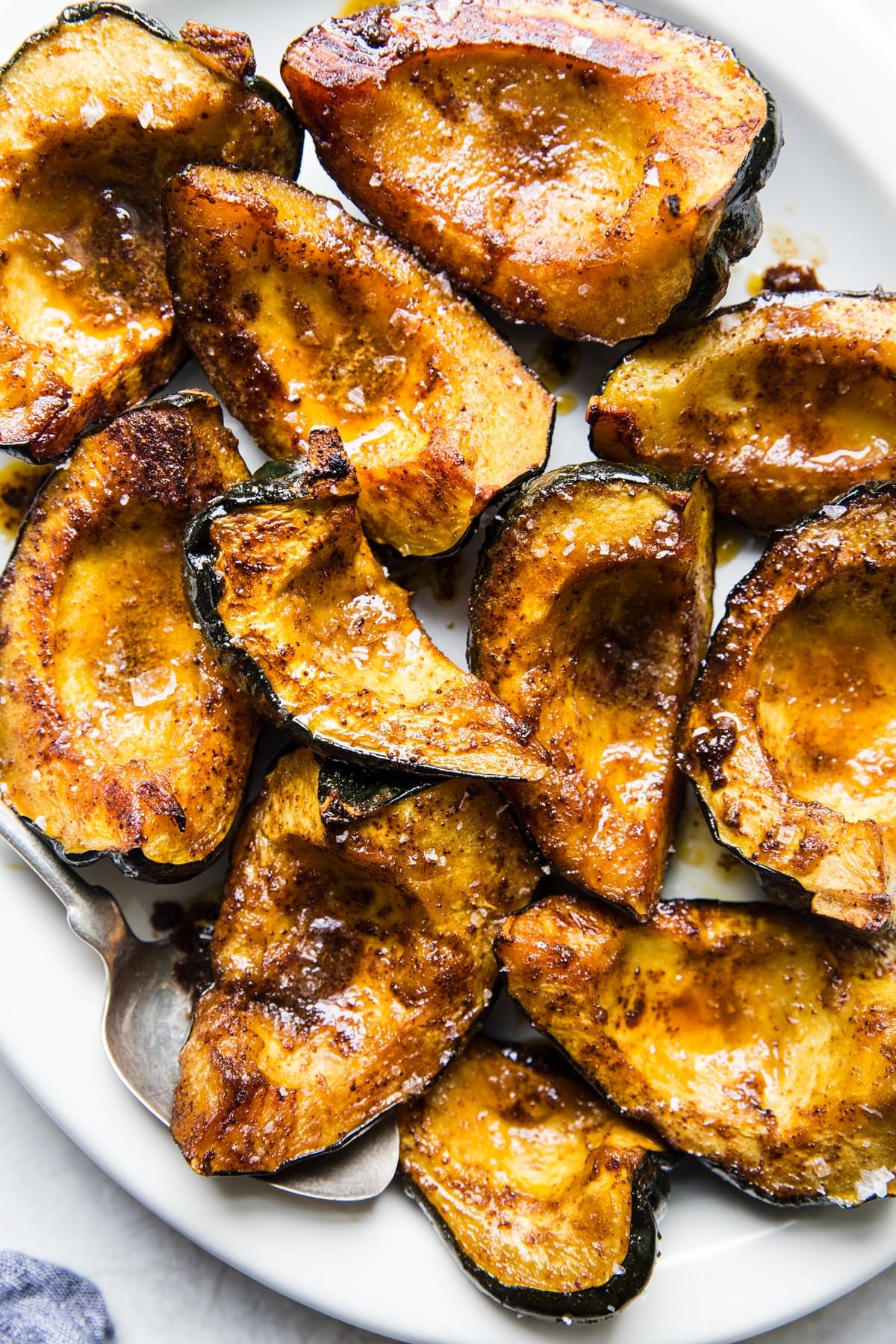 quartered roasted acorn squash on a white platter with a large serving spoon