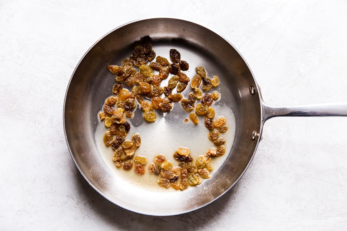Golden raisins in vinegar and chicken stock in a stainless steel skillet