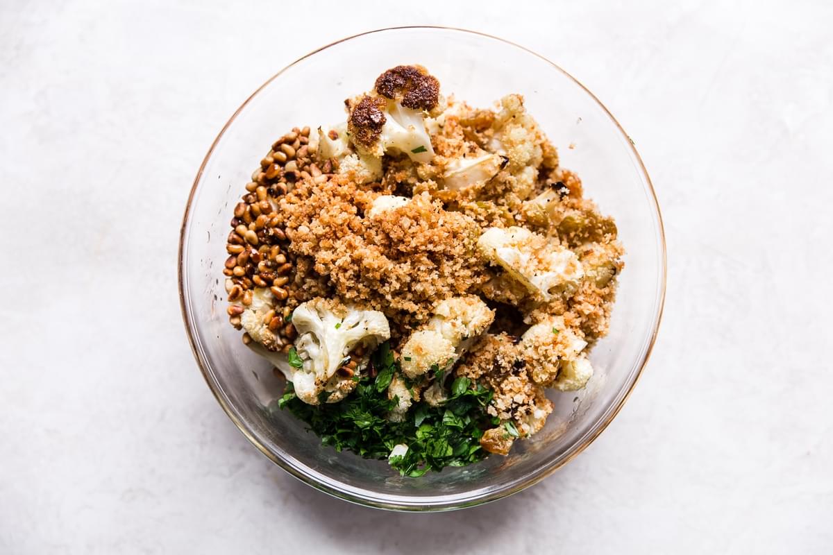 Roasted cauliflower, toasted panko bread crumbs, golden raisins, pine nuts and parsley in a bowl.