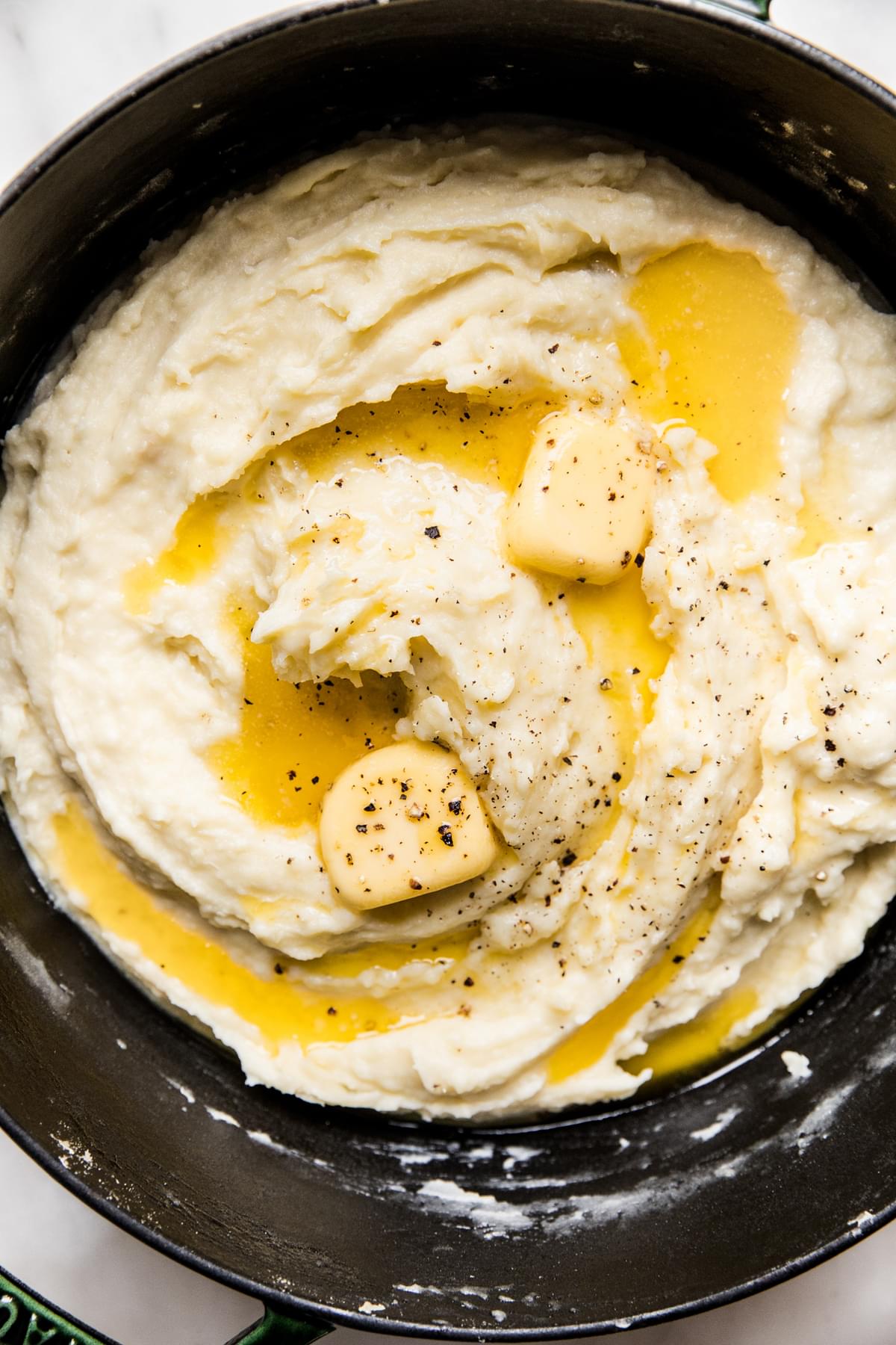 Roasted garlic mashed potatoes topped with melted butter and black pepper in a pot