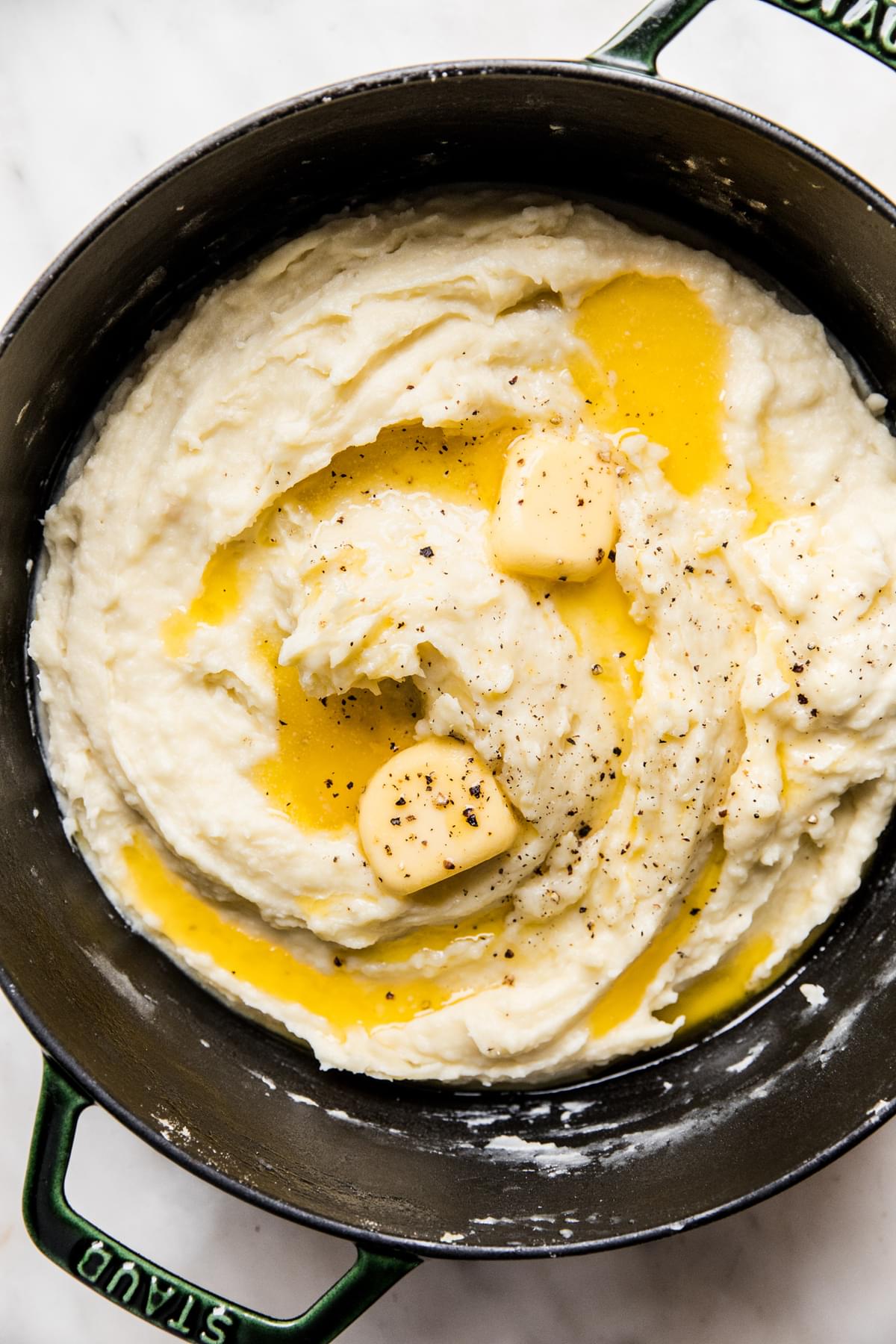 A pot filled with roasted garlic mashed potatoes topped with melted butter and black pepper