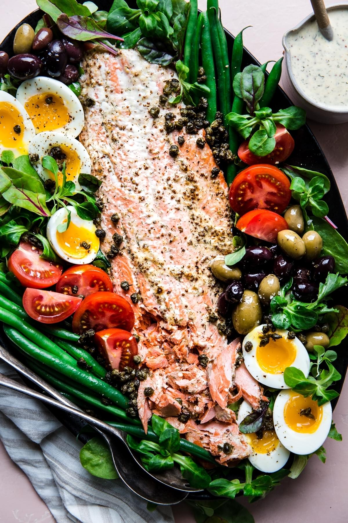 Salmon Niçoise Salad on a platter with olives, tomatoes, green beans, fried capers and soft boiled eggs.
