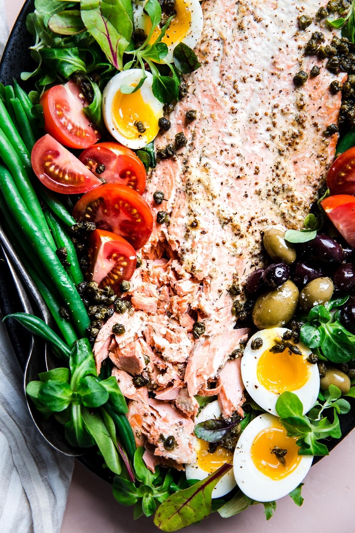 salmon nicoise on a large platter with eggs, green beans, tomatoes, olives and capers