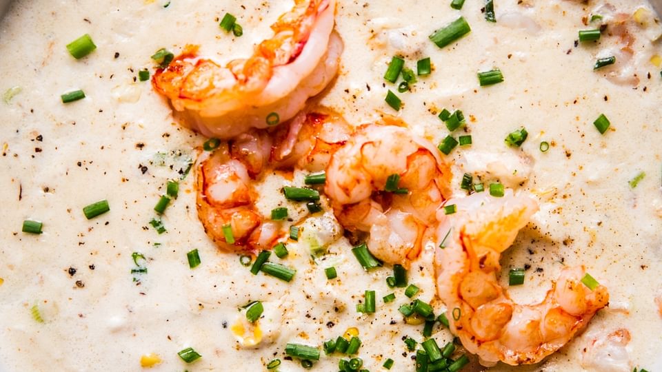 seafood bisque topped with fresh shrimp and chives in a white bowl
