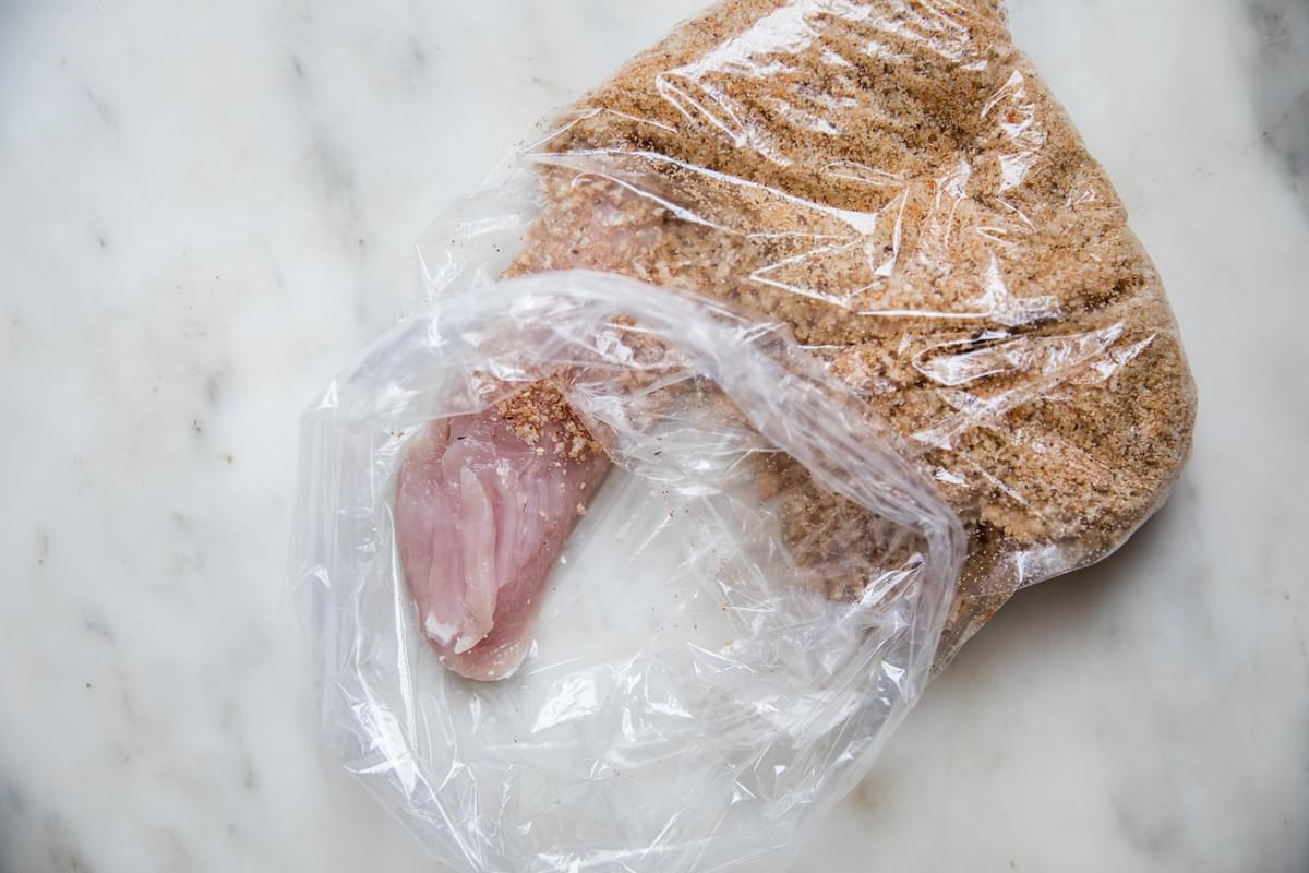 raw chicken in a plastic bag being coated with breadcrumbs and spices to make homemade shake and bake chicken