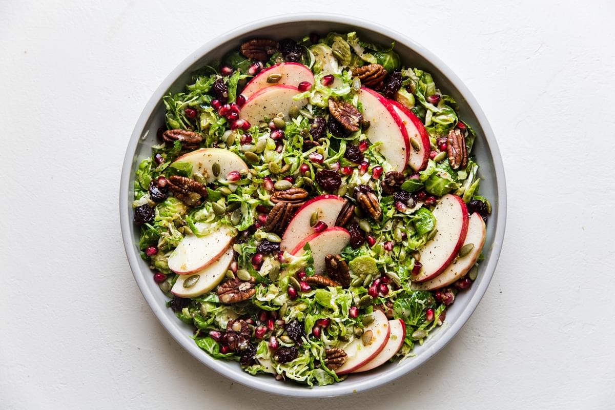 large bowl filled with shaved Brussels sprout salad a creamy maple dressing, apples, pumpkin seeds, dried cherries and pecans