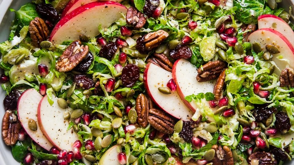shaved brussels sprout salad in a large bowl topped with apples, pecans, cherries, pumpkin seeds and pecans