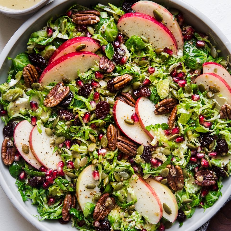 shaved brussels sprout salad in a large bowl topped with apples, pecans, cherries, pumpkin seeds and pecans