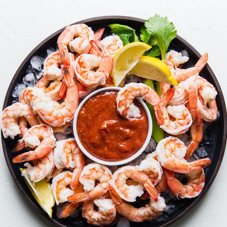 shrimp cocktail sauce with shrimp over ice on a black plate