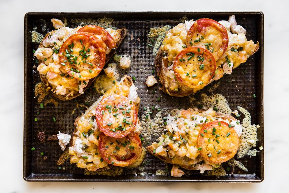 four open faced shrimp melts on a baking sheet topped with fresh chives