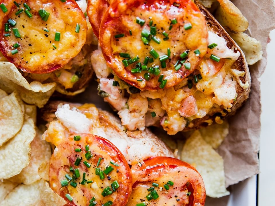 three open faced shrimp melts topped with fresh tomato slices and fresh chives on a tray surrounded by potato chips