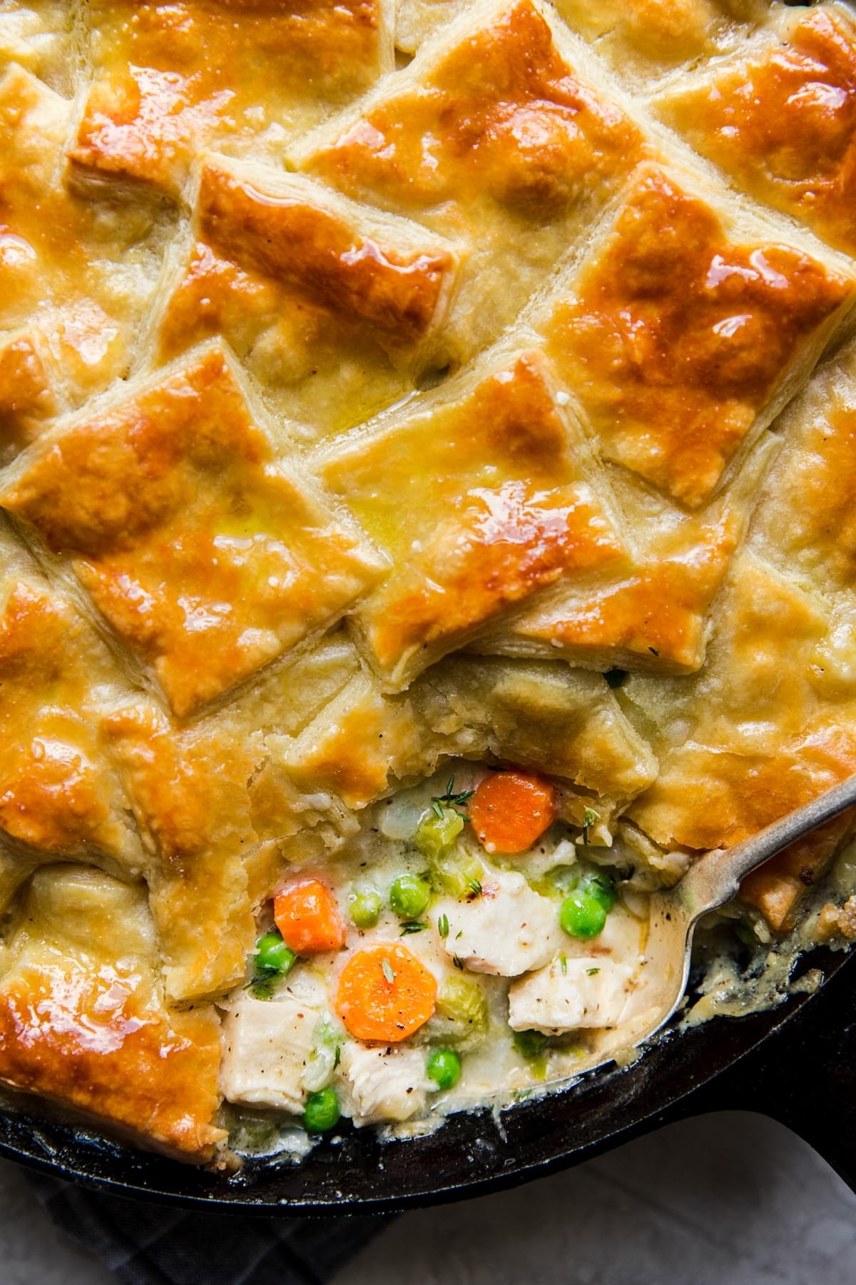 golden brown homemade Chicken Pot Pie in a cast iron pan with a scoop taken out with a spoon.