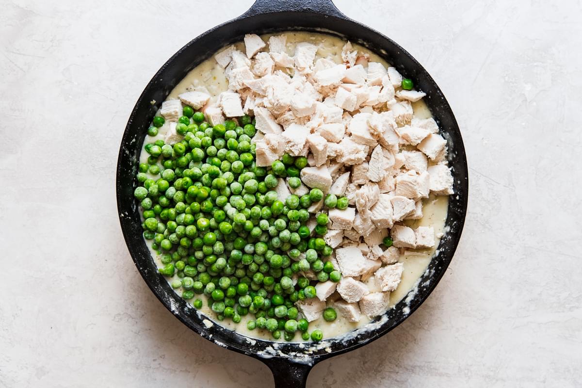 chicken and frozen peas being added a homemade chicken pot pie in a cast iron skillet