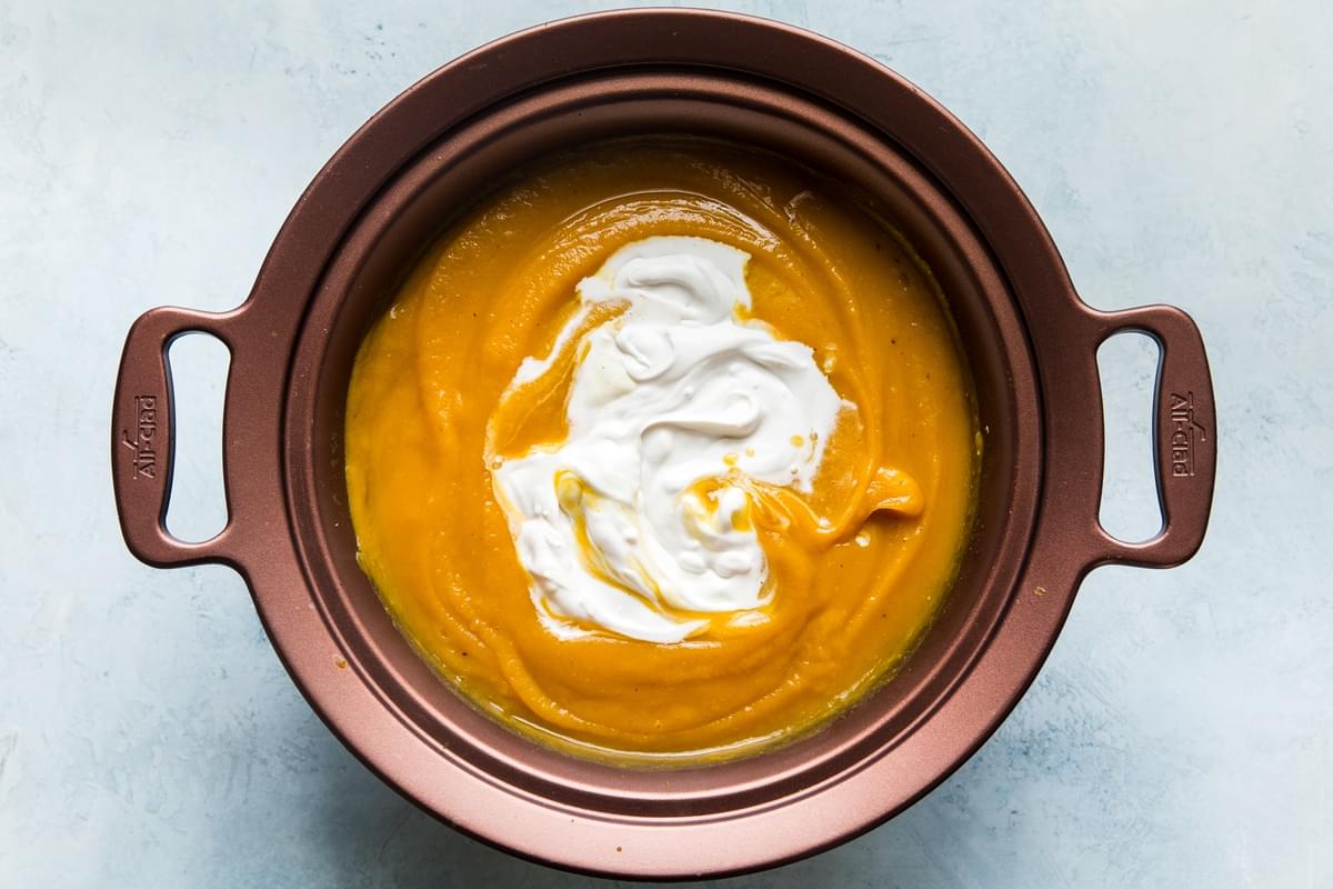 butternut squash soup pureed in a slow cooker topped with coconut milk
