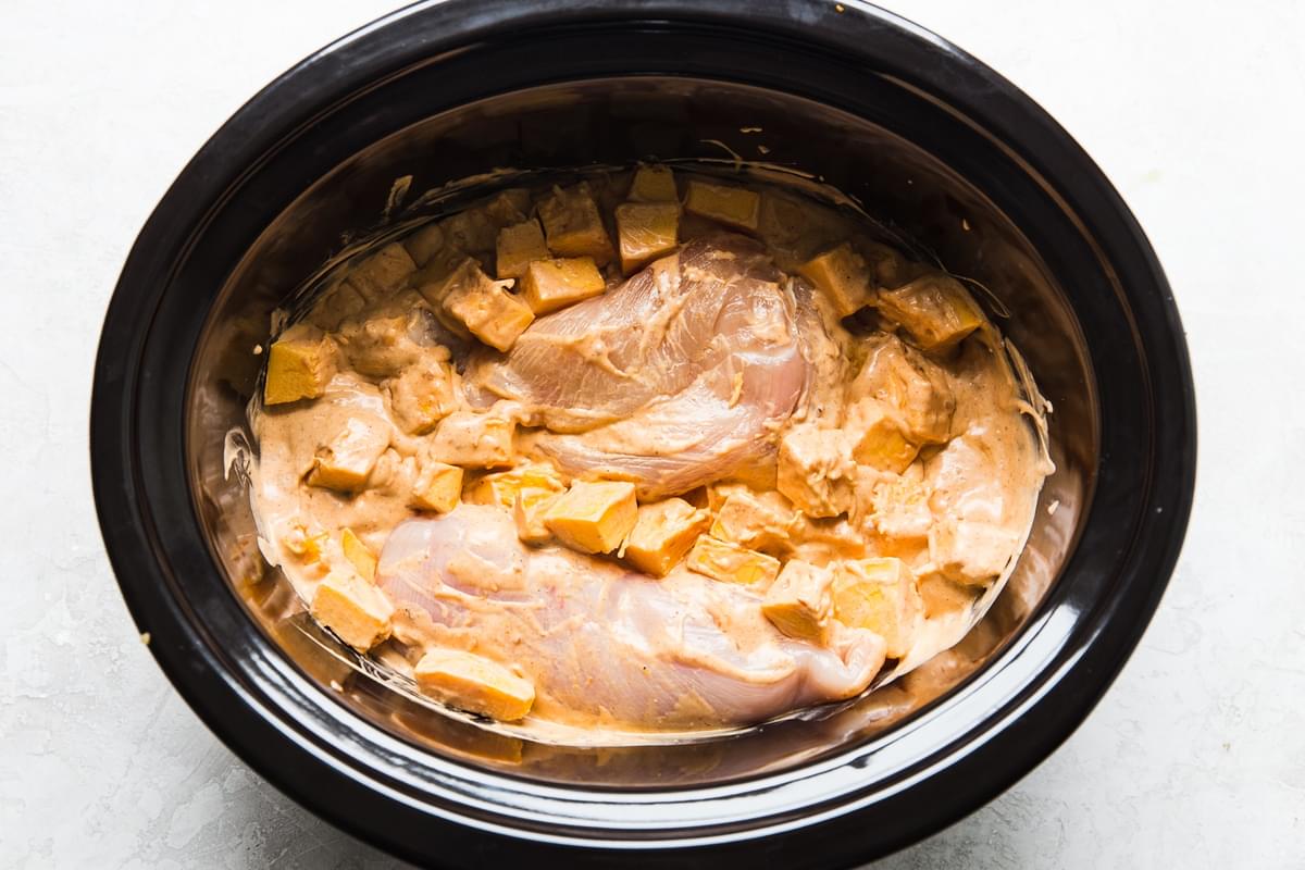raw chicken breasts and cubed pumpkin stirred with red curry and coconut milk in a slow cooker