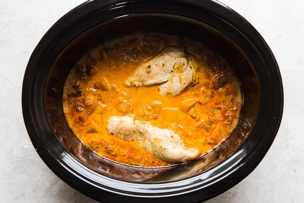 pumpkin curry in a slow cooker with whole cooked chicken breasts