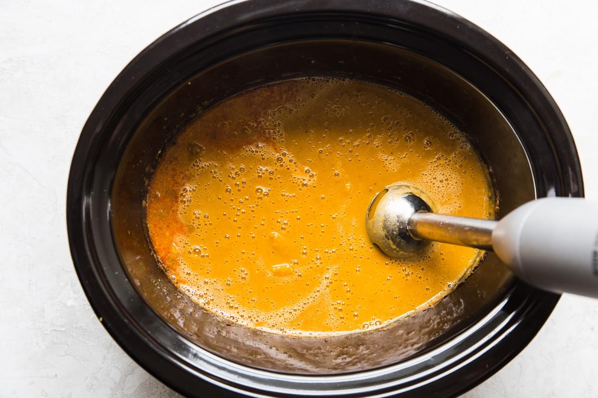 crock pot of pumpkin red curry being blended with an immersion blender