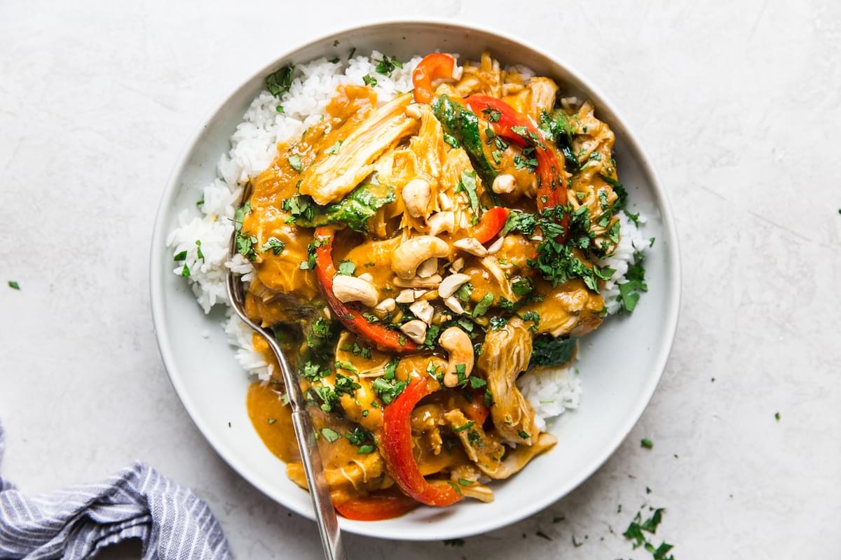 slow cooker pumpkin chicken curry in a bowl over white rice topped with cilantro and cashews