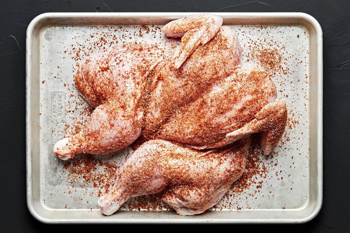 a raw spatchcocked chicken on a baking sheet coated in brown sugar, paprika, garlic powder, pepper and salt