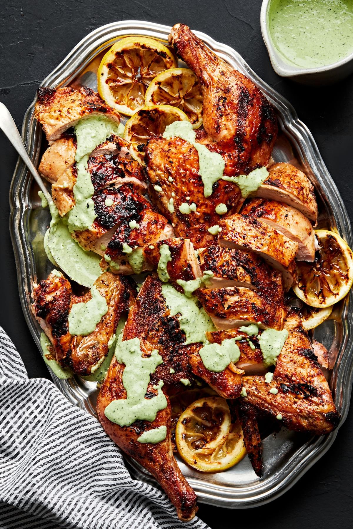 spatchcocked grilled chicken on a serving platter drizzled with homemade herb sauce