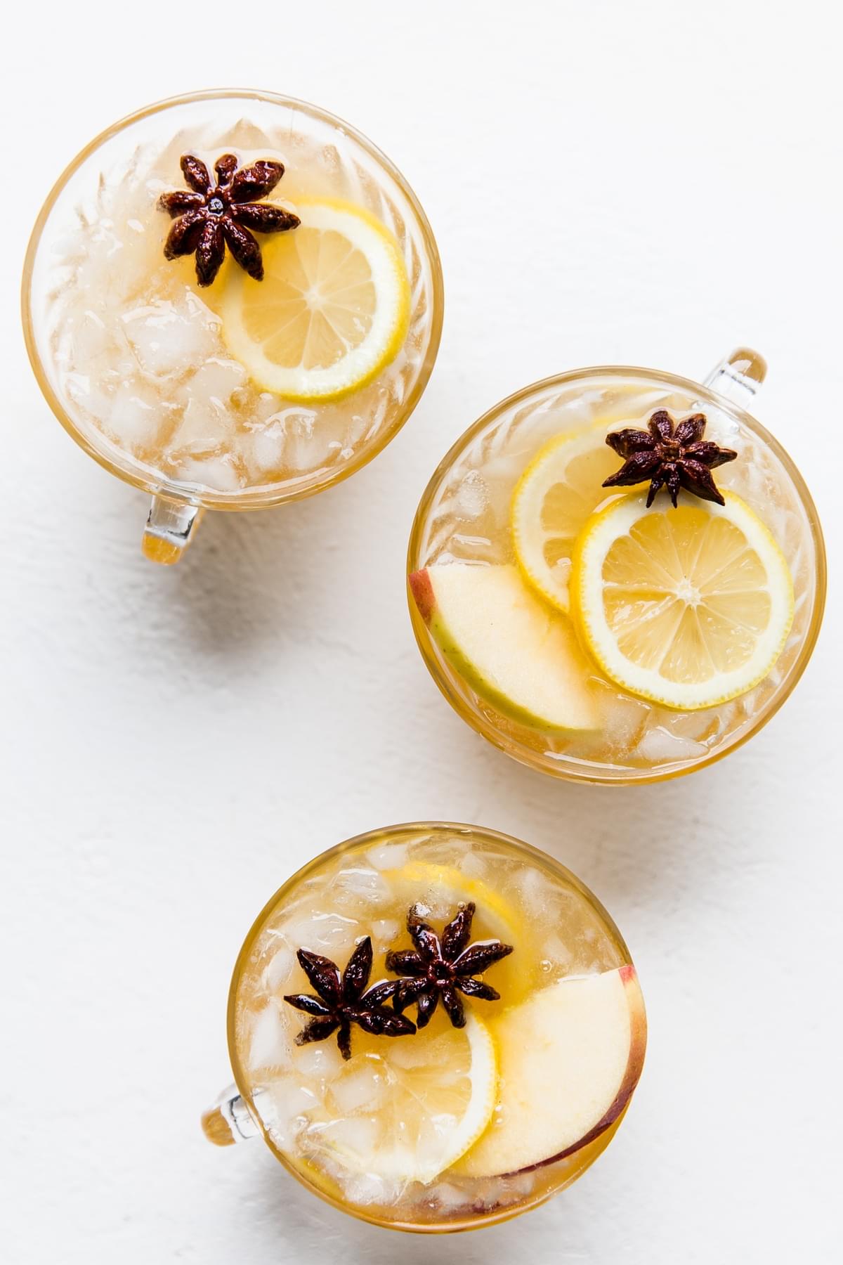 three punch cups with spiced bourbon and crushed ice topped with lemon slices, star anise and apple slices