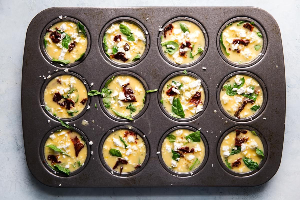 uncooked egg cups with feta, spinach and sun-dried tomato  in a muffin tin ready for the oven