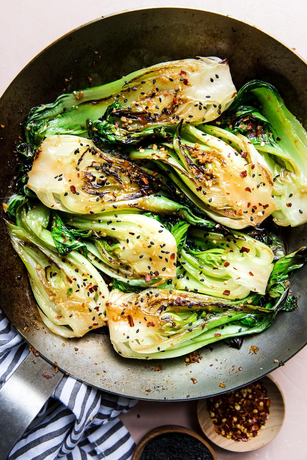 stir fried bok choy in a skillet topped with sesame seeds and red pepper flakes