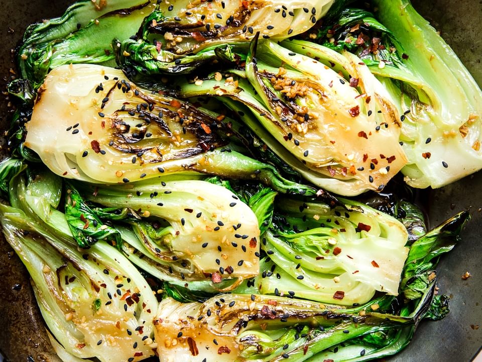 stir fried bok choy with garlic soy sauce and sesame seeds in a skillet