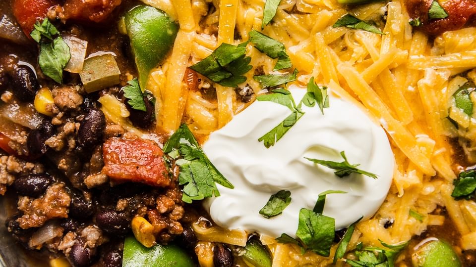 a bowl of homemade taco soup made with ground beef and black beans topped with cheddar cheese, sour cream and fresh cilantro