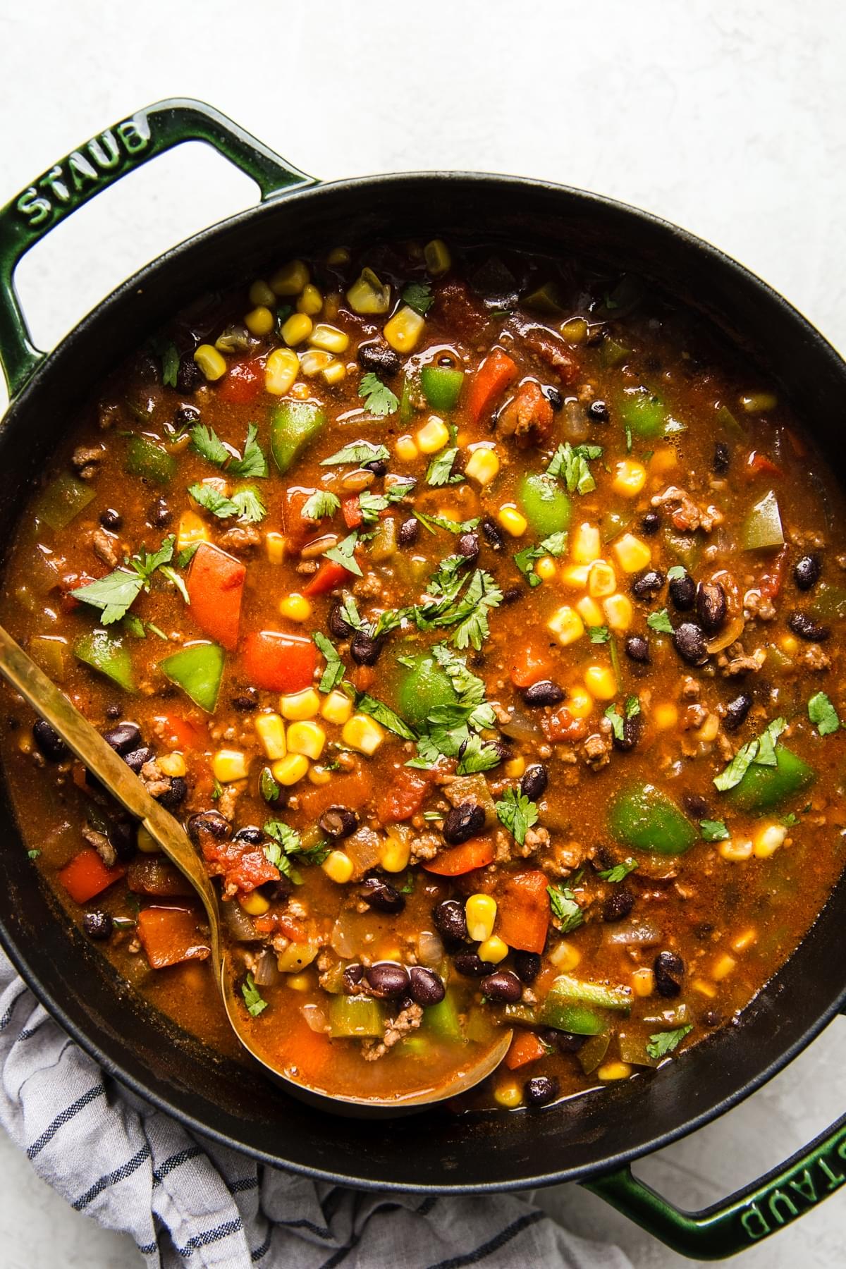 a pot of homemade taco soup made with ground beef, black beans, corn and bell pepper being scooped with a ladle