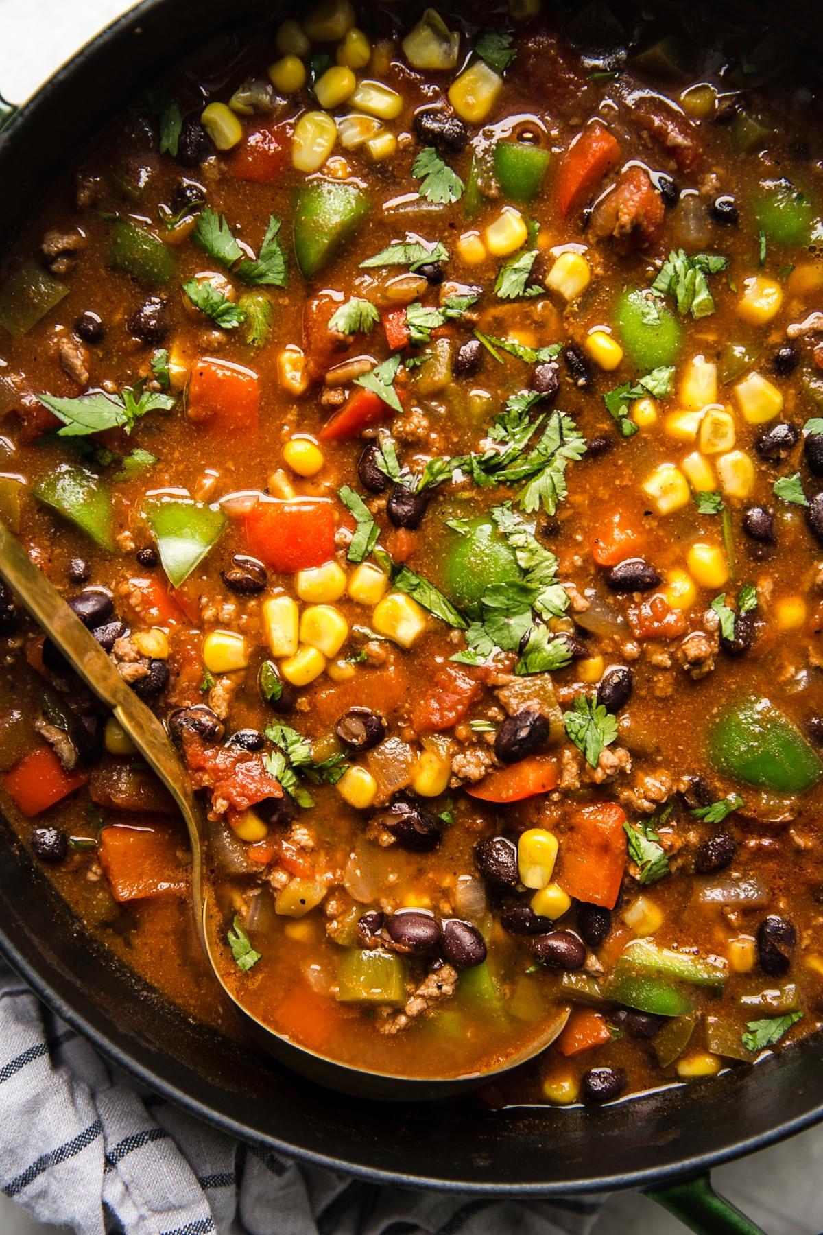 a pot of homemade taco soup made with ground beef, black beans, corn and bell pepper being scooped with a ladle