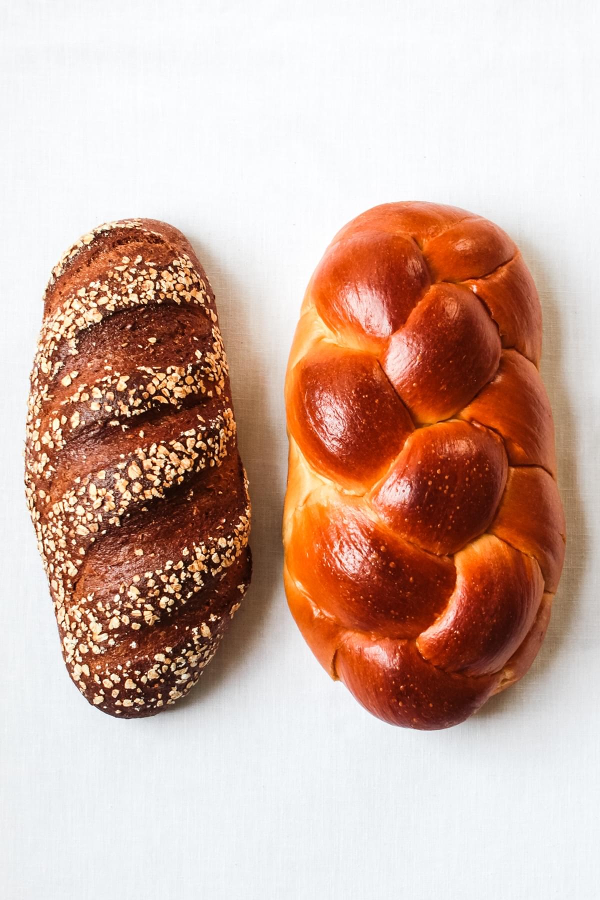 loaf of seeded whole wheat bread next to a loaf of challah bread