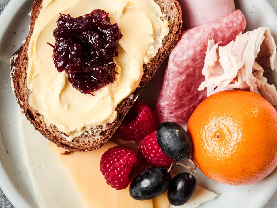 plate of bread with butter and jam, fresh fruit, cold cut meats and and mild cheeses