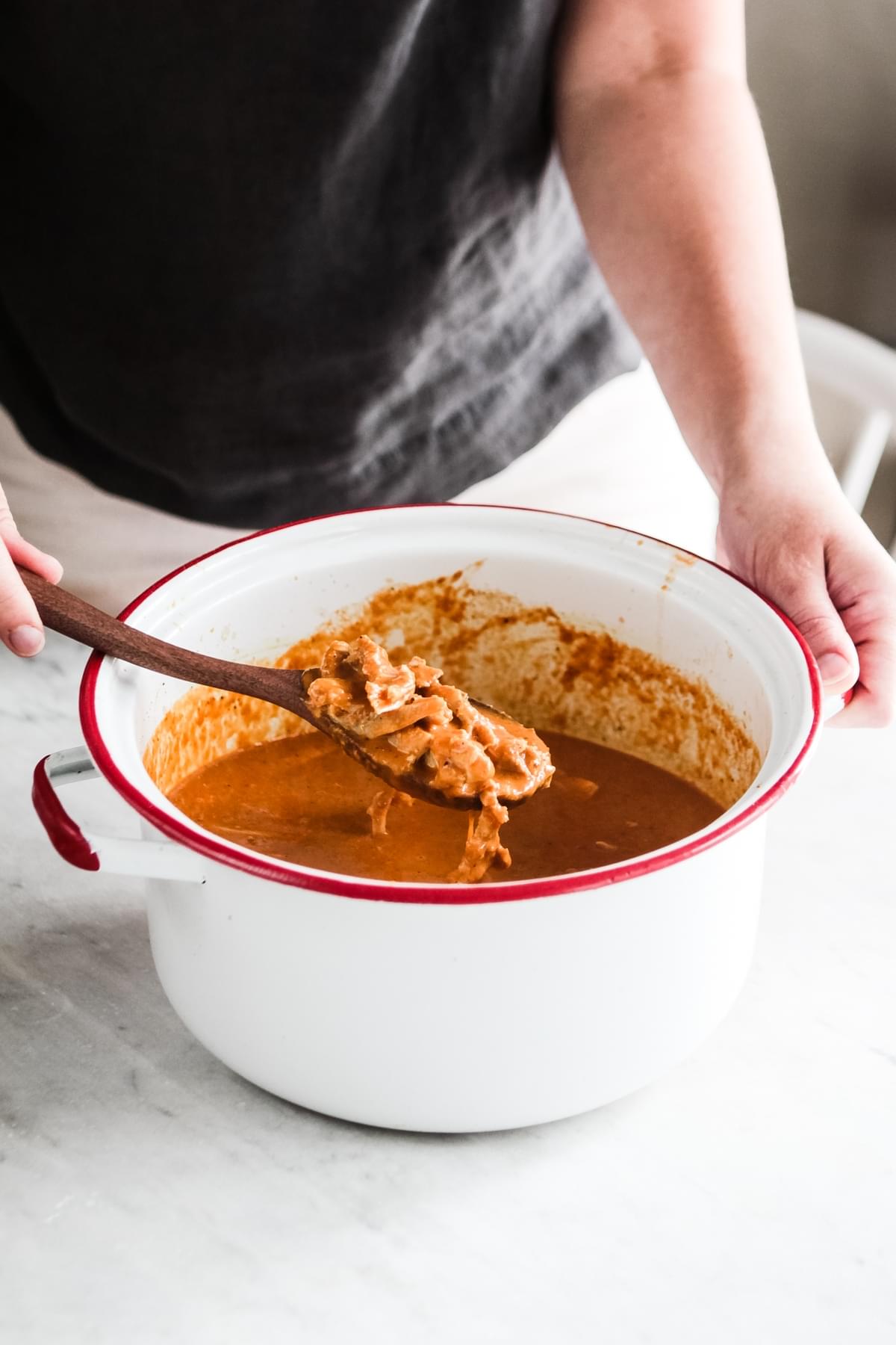 hands scooping chicken out of a pot of tikka masala soup with a wooden spoon