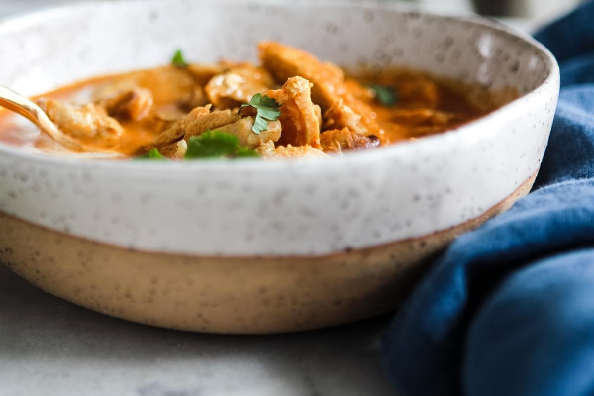 speckled ceramic bowl of tikka masala soup with a blue linen