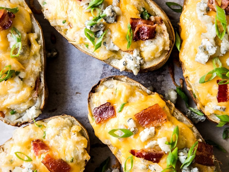 close up of twice baked potatoes topped with melted cheddar cheese, crispy bacon, fresh scallions, and blue cheese