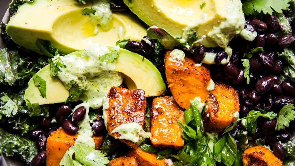 vegan roasted sweet potato and kale salad with black beans and avocado in a bowl with cashew cilantro dressing