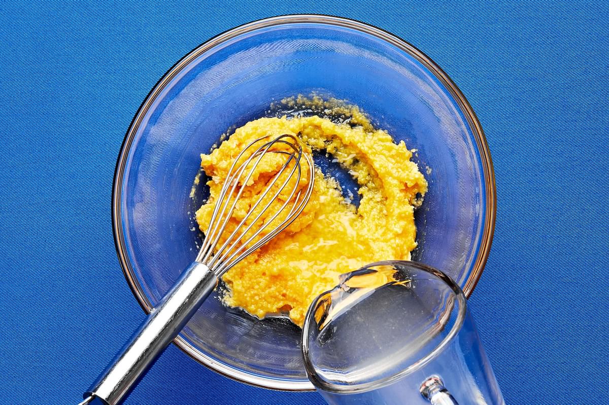 reserved pasta water being poured into a glass bowl with whisked eggs and parmesan cheese