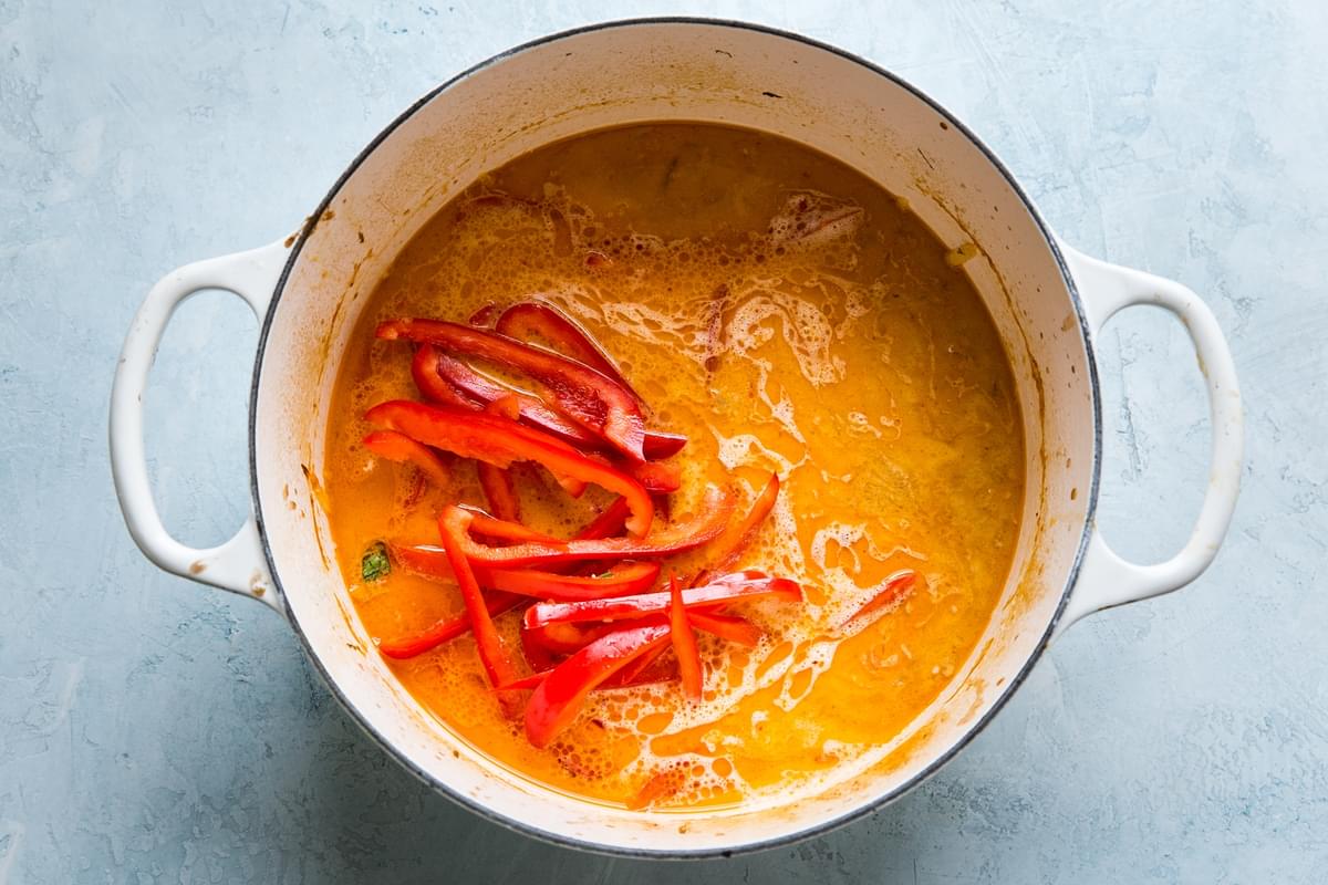 red curry coconut broth in a large soup pot with red bell pepper slices