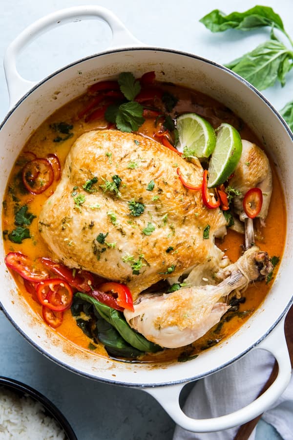 Whole Poached Chicken In Coconut Curry in a soup pot with basil and lime