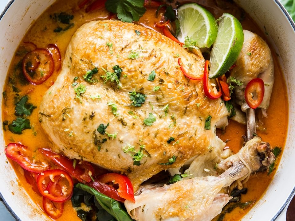 Whole Poached Chicken In Coconut Curry in a soup pot with basil and lime