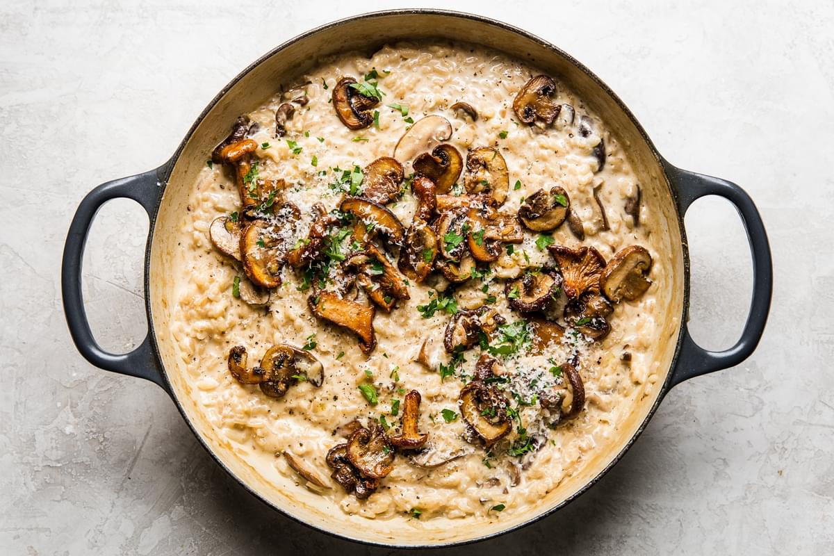 wild mushroom risotto in a skillet topped with grated parmesan cheese and fresh parsley