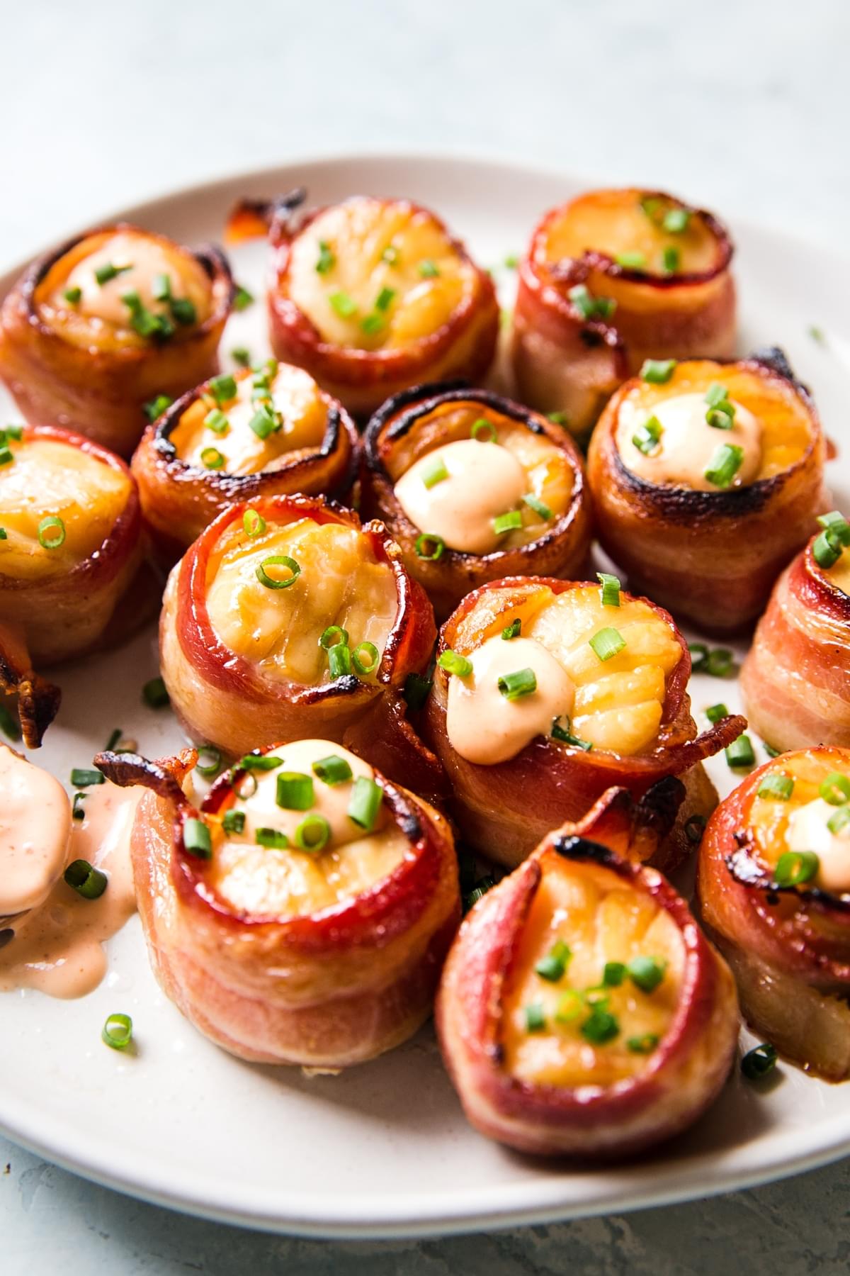 bacon wrapped scallop recipe on a white plate with sriracha aioli and fresh chives
